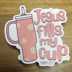 May include: Pink and white sticker with a pink cup with a straw and white daisies. The text reads "Jesus fills my cup" with the scripture reference "PSALM 23:5" below.