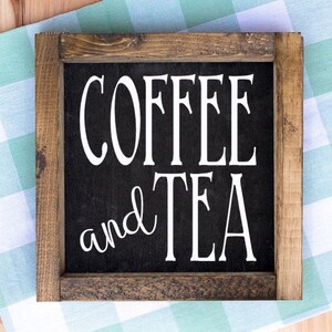 May include: Square wooden sign with the words "COFFEE and TEA" in white lettering on a black background. The sign has a dark brown wooden frame and is set against a green and white checkered cloth.