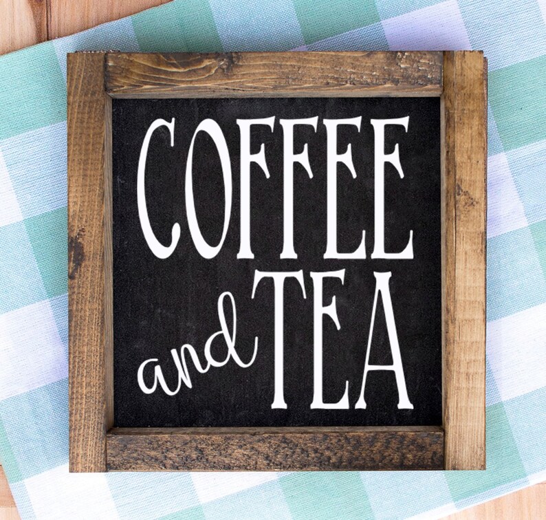 May include: Square wooden sign with the words "COFFEE and TEA" in white lettering on a black background. The sign has a dark brown wooden frame and is set against a green and white checkered cloth.