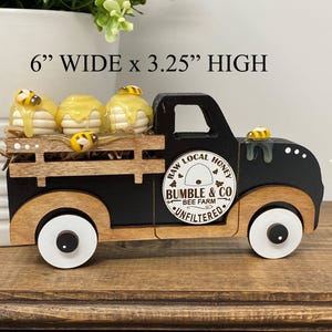 May include: A black and wood-toned decorative truck carrying three honey-covered treats and bee figurines. The truck is 15.24 cm wide and 8.26 cm high, with the text "RAW LOCAL HONEY" and "BUMBLE & CO BEE FARM UNFILTERED" on the side.