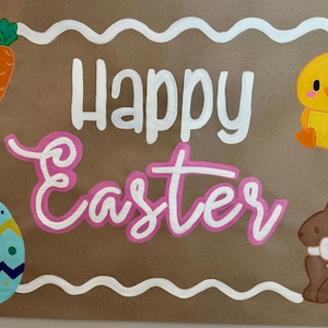 May include: A brown rectangular sign with the words "Happy Easter" in white and pink. The sign is decorated with a yellow chick, a brown bunny with a pink bow, carrots, and a decorated egg.