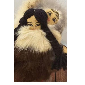 Op de afbeelding: Handgemaakte pop met een vrouw met zwart garen haar en een met bont afgezette jas. Een kleinere pop is aan de achterkant bevestigd. Het gezicht van de pop is met de hand beschilderd met delicate kenmerken. De vacht is een mix van bruin, crème en grijs.