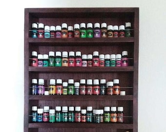 May include: A dark wood wall shelf with six shelves, each holding rows of small glass bottles with colorful liquids. The bottles are arranged in a rainbow pattern. The shelf is mounted on a white wall.