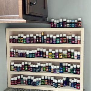 May include: A wooden shelf unit with four tiers, each holding rows of small glass bottles with colourful liquids. The bottles are neatly organised and labelled, suggesting they contain essential oils.