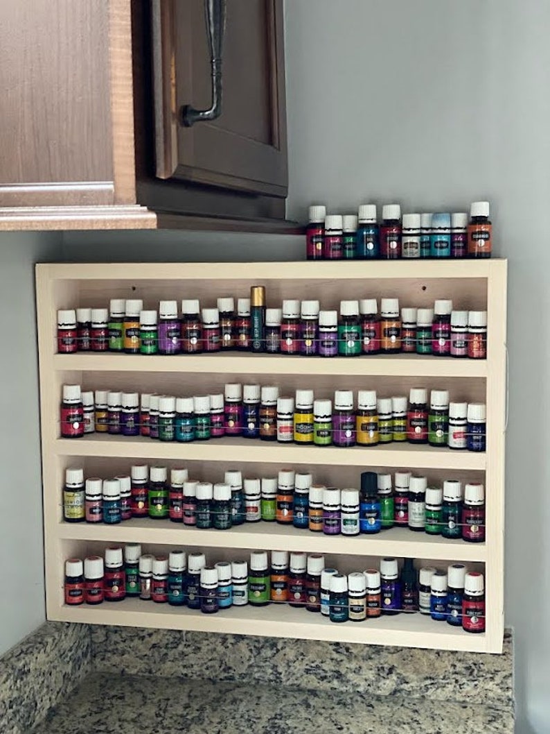 May include: A wooden shelf unit with four tiers, each holding rows of small glass bottles with colourful liquids. The bottles are neatly organised and labelled, suggesting they contain essential oils.