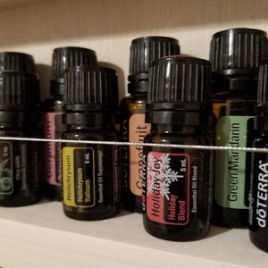 May include: A shelf with a variety of essential oil bottles, including Grapefruit, Helichrysum Italicum, Holiday Joy, and Green Mandarin. The bottles are all 5 ml and are labelled with the dōTERRA brand.