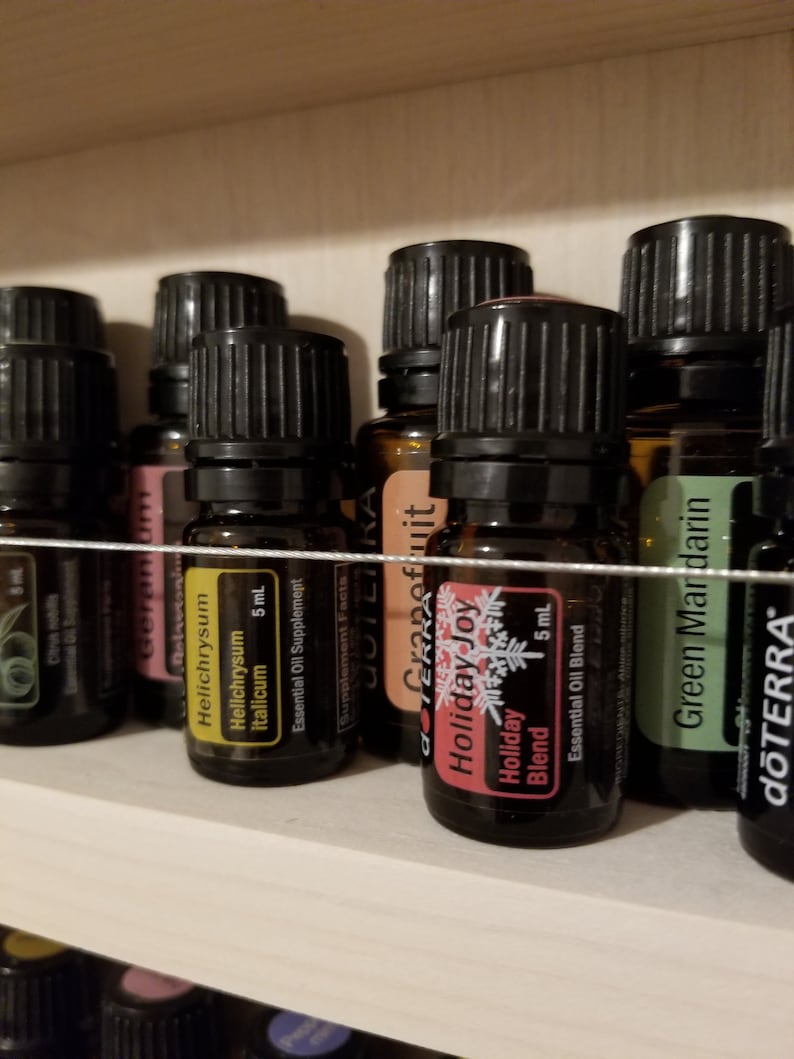 May include: A shelf with a variety of essential oil bottles, including Grapefruit, Helichrysum Italicum, Holiday Joy, and Green Mandarin. The bottles are all 5 ml and are labelled with the dōTERRA brand.