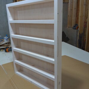 May include: White wooden spice rack with six shelves and wire dividers. The rack is unfinished and has a natural wood grain.