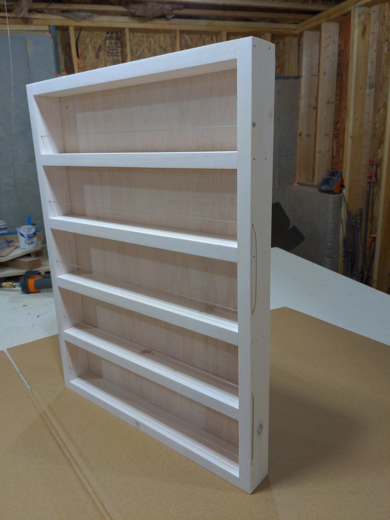 May include: White wooden spice rack with six shelves and wire dividers. The rack is unfinished and has a natural wood grain.