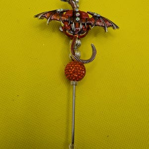 May include: A silver and red dragon-shaped bottle stopper with a crystal-like finish. The dragon has wings and a tail that curls around a red crystal ball.