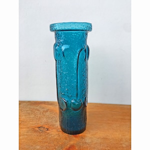 May include: A teal blue glass vase with a textured surface and a unique design. The vase has a cylindrical shape and a wide mouth.
