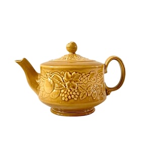Könnte beinhalten: Eine braune Teekanne aus Keramik mit einem Blumendesign. Die Teekanne hat einen runden Korpus und einen Deckel mit einem Knopf. Das Design zeigt Trauben, Blätter und Blumen.