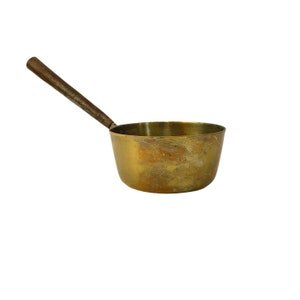 Puede incluir: Una olla de cobre con un mango de madera. La olla tiene un aspecto desgastado y antiguo y es un utensilio de cocina tradicional.