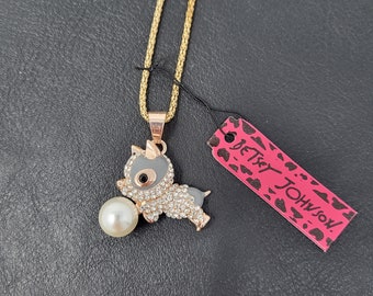 Può includere: Una collana con catena dorata con un ciondolo animale grigio e bianco che tiene una perla. Il ciondolo è ricoperto di strass. L'etichetta attaccata alla collana recita "Betsy Johnson".