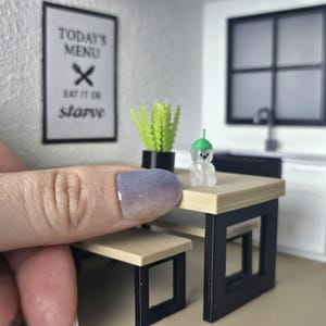 May include: Miniature dining set with a table, bench, and a small bear figurine wearing a green hat. A framed sign reads "TODAY'S MENU: EAT IT OR starve". A green plant in a black pot is also on the table.