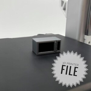 Può includere: Un modello di forno a microonde piccolo di colore grigio stampato in 3D. Il modello misura circa 5 cm di altezza e 7,5 cm di larghezza. Il forno a microonde ha una porta nera con una maniglia. Il modello è seduto su una superficie grigia. FILE DI STAMPA 3D.