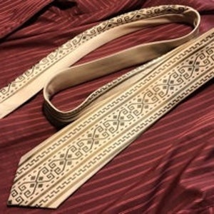 May include: A beige silk tie with a brown and black geometric pattern. The pattern is a repeating design of squares and diamonds.