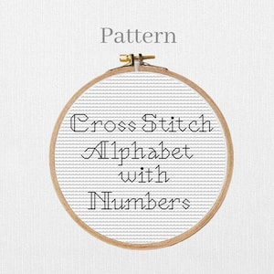 May include: A circular wooden embroidery hoop containing white Aida fabric with black cross-stitched text that reads Pattern, Cross Stitch, Alphabet, with, Numbers. The hoop features a metal tension screw at the top for securing the fabric.