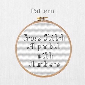Può includere: Un telaio da ricamo circolare in legno contenente tessuto Aida bianco con scritte a punto croce nero che recitano Pattern Cross Stitch Alphabet with Numbers. Il disegno è centrato nel telaio, dotato di una vite di serraggio in metallo.