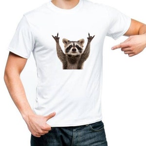 May include: White t-shirt with a graphic of a raccoon making a rock and roll hand gesture.
