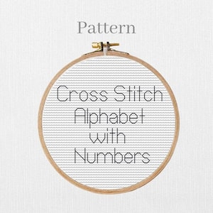 May include: A wooden embroidery hoop holding a cross-stitch pattern. The pattern features the text "Cross Stitch Alphabet with Numbers" in black against a gray background. The word "Pattern" is above the hoop.