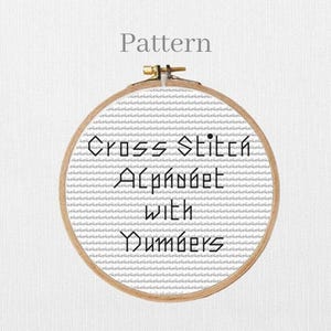 May include: A cross-stitch pattern in a wooden embroidery hoop. The text "Cross Stitch Alphabet with Numbers" is displayed in black. The word "Pattern" is above the hoop.