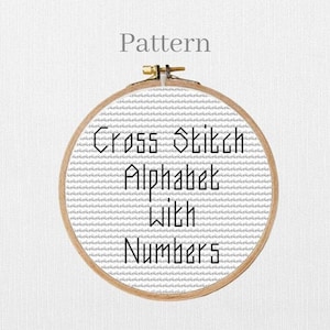May include: A cross-stitch pattern in a wooden embroidery hoop. The pattern features the words "Cross Stitch Alphabet With Numbers" in black text on a white background. The word "Pattern" is above the hoop.