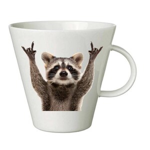 May include: White ceramic coffee mug with a raccoon wearing a mischievous expression and giving the peace sign with both hands. The raccoon is printed on the mug.
