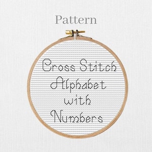 May include: A cross-stitch pattern in a wooden embroidery hoop. The text "Cross Stitch Alphabet with Numbers" is stitched in black thread on a gray fabric background. The word "Pattern" is above the hoop.