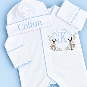 Peut inclure: Une grenouill&egrave;re blanche &agrave; manches longues avec pieds et un bonnet assorti, orn&eacute;s d'un liser&eacute; festonn&eacute; bleu clair. Le bonnet porte le pr&eacute;nom brod&eacute; Colton. La grenouill&egrave;re pr&eacute;sente un &eacute;cusson brod&eacute; avec les initiales CHK et deux cerfs.
