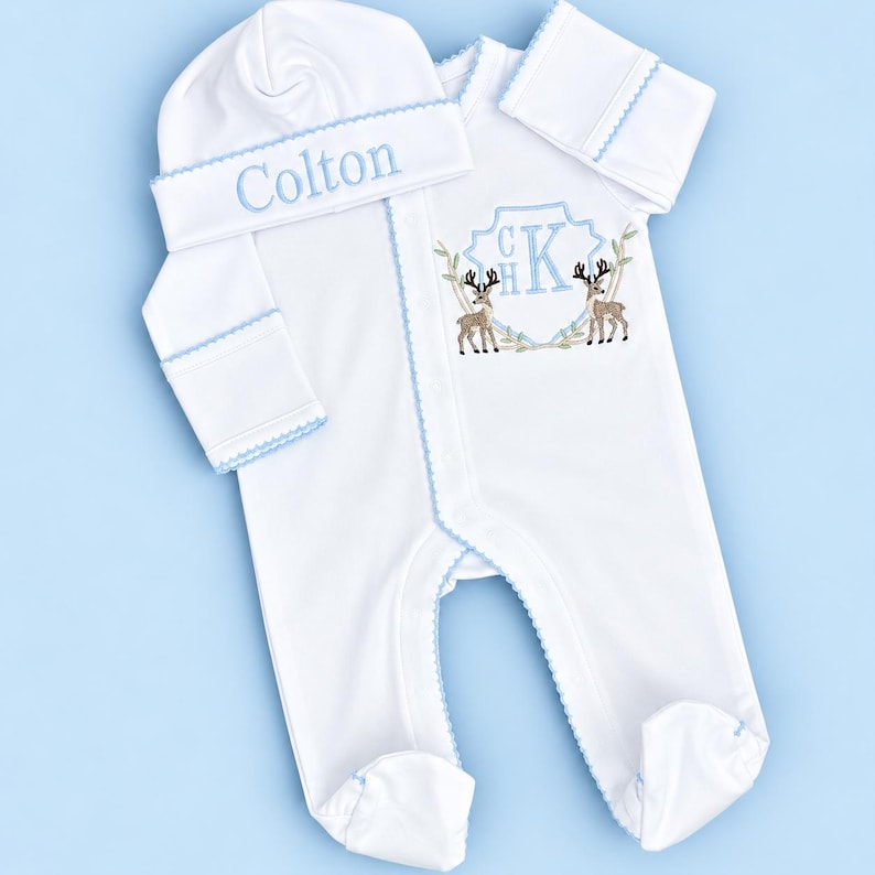 Peut inclure: Une grenouill&egrave;re blanche &agrave; manches longues avec pieds et un bonnet assorti, orn&eacute;s d'un liser&eacute; festonn&eacute; bleu clair. Le bonnet porte le pr&eacute;nom brod&eacute; Colton. La grenouill&egrave;re pr&eacute;sente un &eacute;cusson brod&eacute; avec les initiales CHK et deux cerfs.