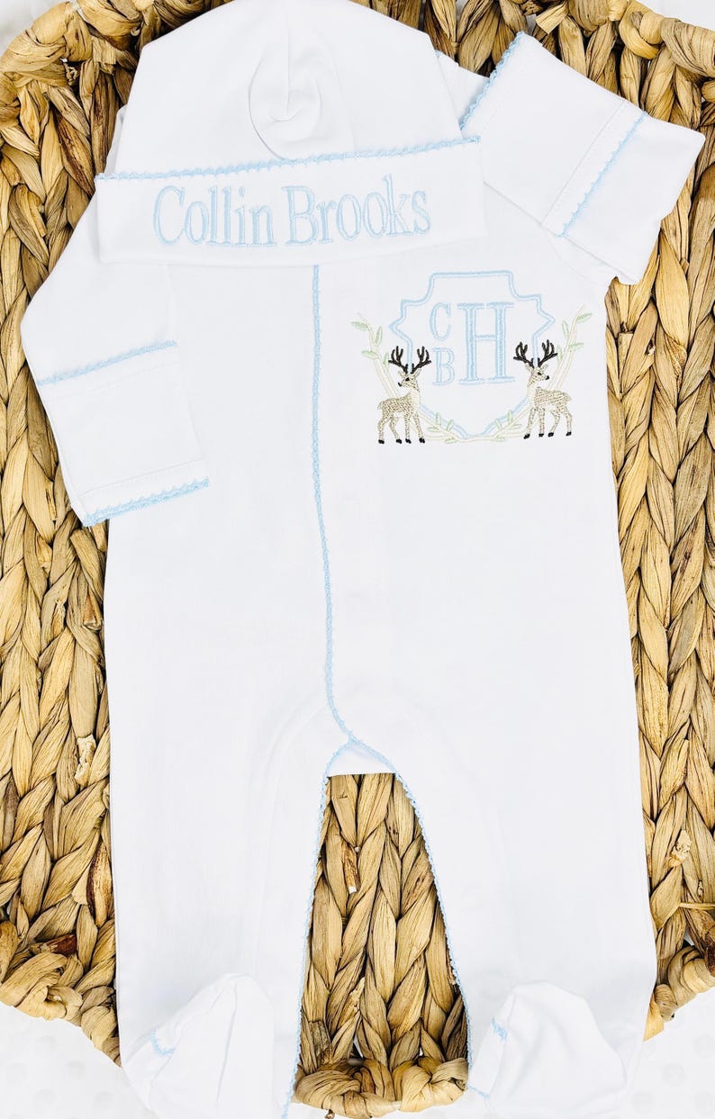 Peut inclure: Un ensemble pyjama blanc &agrave; manches longues avec pieds et bonnet assorti, dot&eacute; d'un liser&eacute; bleu clair. Le bonnet porte le nom brod&eacute; Collin Brooks. Le pyjama pr&eacute;sente un &eacute;cusson brod&eacute; avec les initiales CH et deux cerfs sur la poitrine.