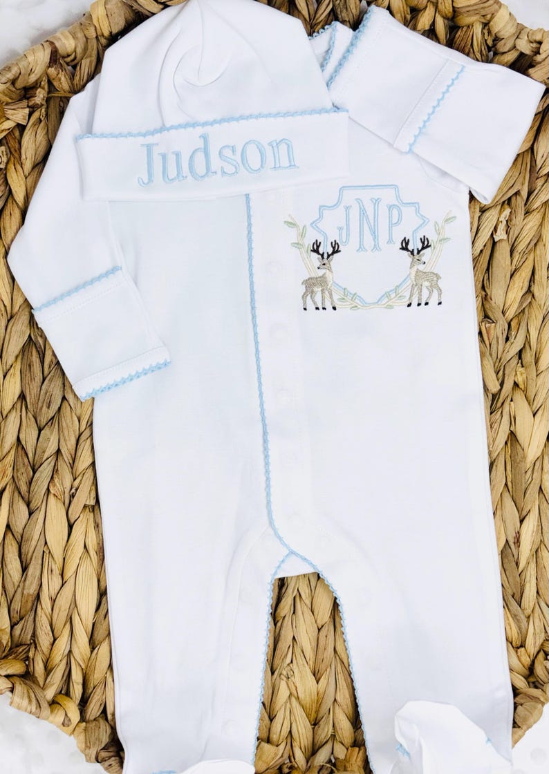 Peut inclure: Une grenouill&egrave;re blanche &agrave; manches longues avec pieds et un bonnet assorti &agrave; bordure bleu clair. Le bonnet porte le nom brod&eacute; Judson. La grenouill&egrave;re pr&eacute;sente un &eacute;cusson brod&eacute; avec les initiales JNP flanqu&eacute;es de deux cerfs marron et gris.