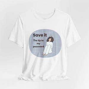 May include: White t-shirt with a graphic design. The design features the text "Save it" above the text "The tip to my password". Below the text is an illustration of a person sitting down. The person is wearing white clothing and has dark curly hair.
