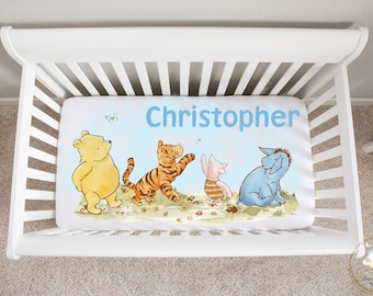 May include: A Winnie the Pooh themed baby cot sheet with a blue background and a white border. The sheet features Winnie the Pooh, Tigger, Piglet, and Eeyore. The name "Christopher" is printed in blue letters at the top of the sheet.