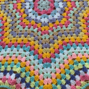 May include: A colorful crochet blanket with a circular pattern in shades of pink, yellow, blue, green, and white.