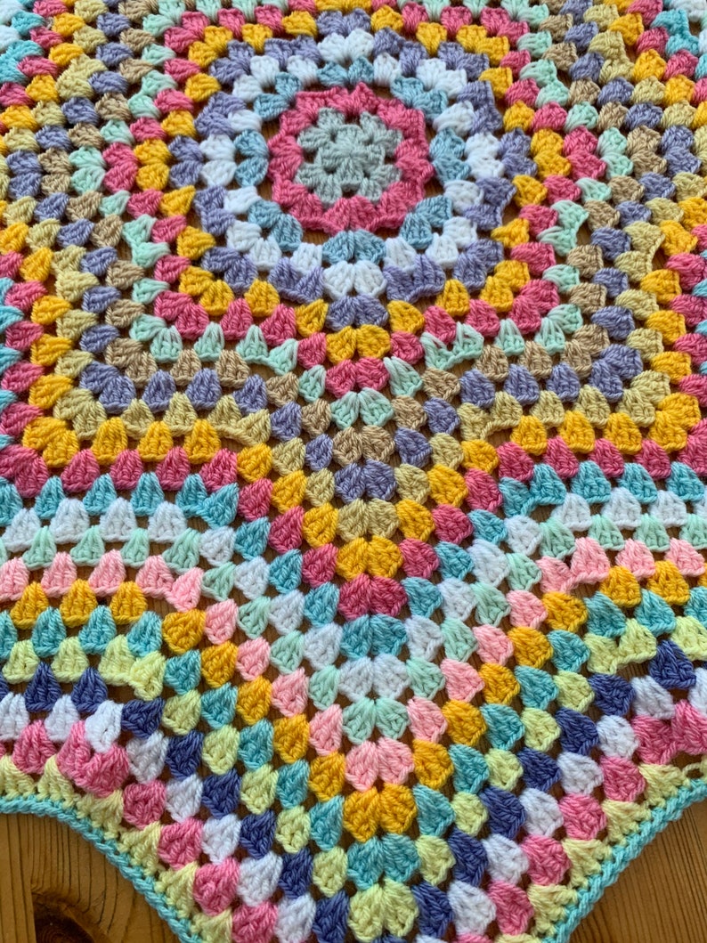 May include: A colorful crochet blanket with a circular pattern in shades of pink, yellow, blue, green, and white.