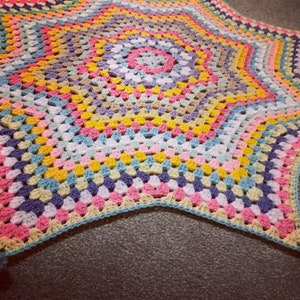 May include: A colorful crocheted star-shaped blanket with a multi-colored center and a light blue border.