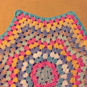 May include: A colorful crocheted blanket with a circular pattern in the center. The blanket is made with a variety of colors, including pink, yellow, blue, and green.