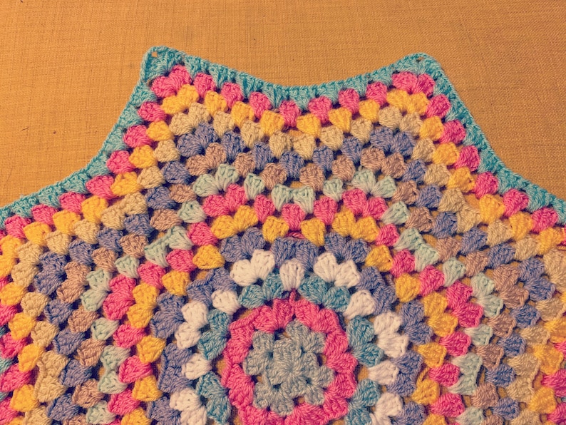 May include: A colorful crocheted blanket with a circular pattern in the center. The blanket is made with a variety of colors, including pink, yellow, blue, and green.