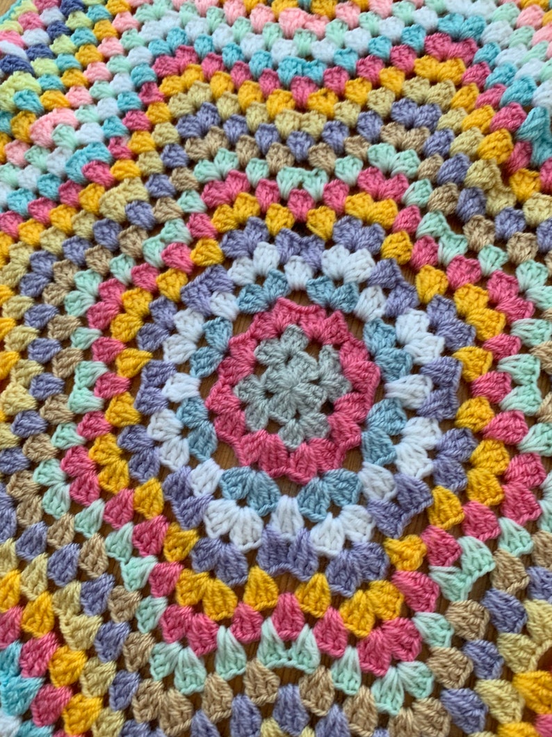 May include: A colorful crocheted blanket with a circular pattern in shades of pink, yellow, blue, green, and purple.