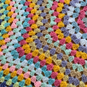 May include: A colorful crocheted blanket with a granny square pattern in shades of pink, yellow, blue, green, and white.