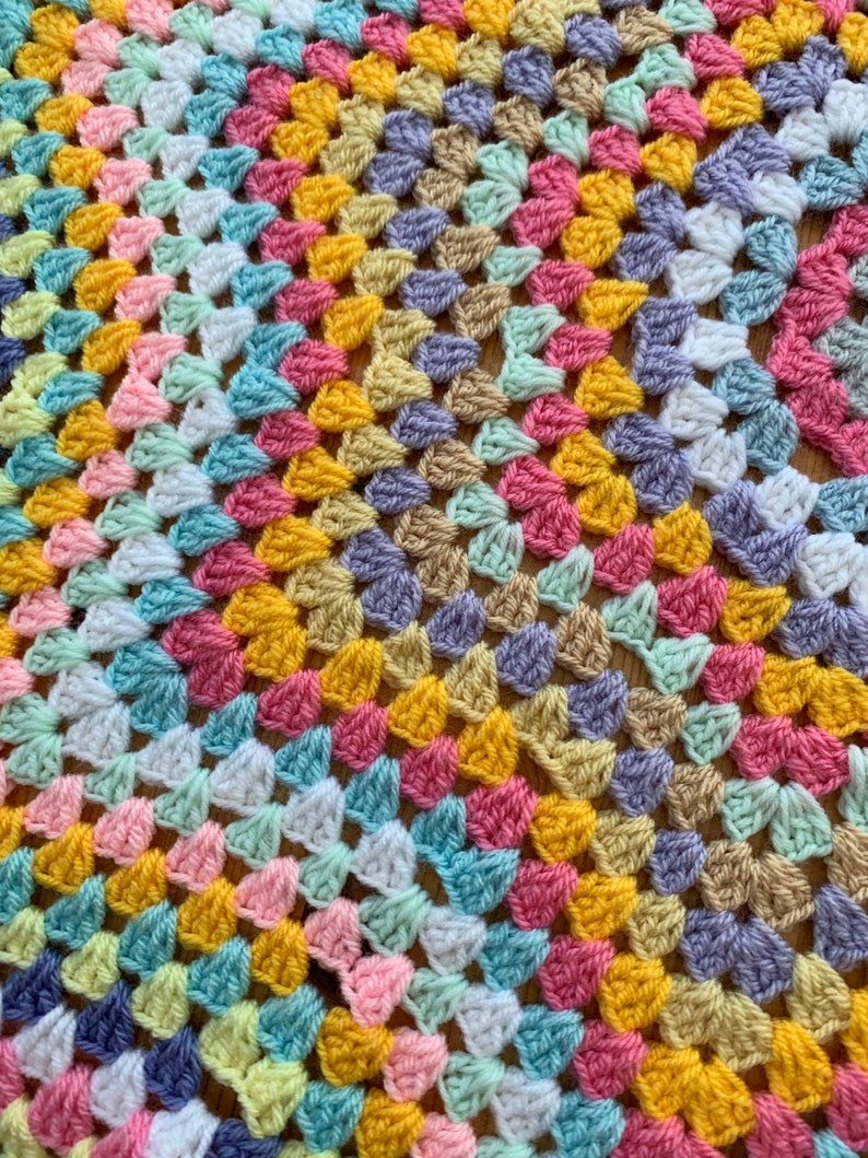 May include: A colorful crocheted blanket with a granny square pattern in shades of pink, yellow, blue, green, and white.