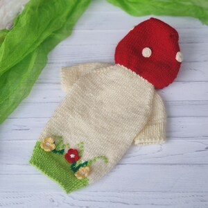 Peut inclure: Une tenue de b&eacute;b&eacute; tricot&eacute;e en forme de champignon. La tenue est de couleur cr&egrave;me avec des accents verts et rouges. Le chapeau de champignon est rouge avec des pois blancs.