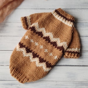 May include: A brown knitted jumper with a white and brown geometric pattern. The jumper has a high neck and long sleeves.
