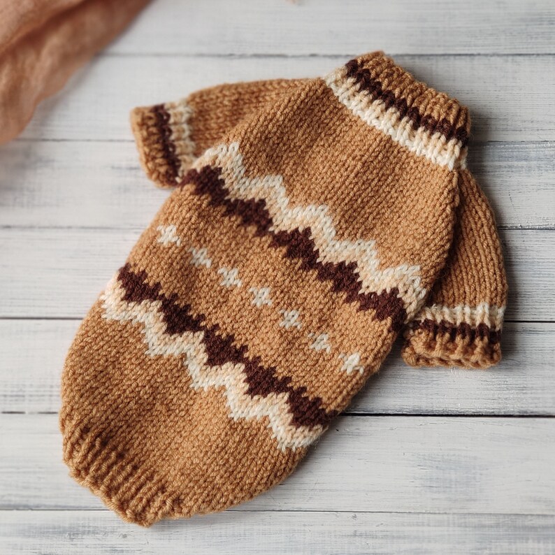 May include: A brown knitted jumper with a white and brown geometric pattern. The jumper has a high neck and long sleeves.