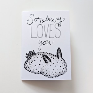 Könnte beinhalten: Eine weiße Karte mit schwarzer Tinte, auf der "Somebunny loves you" steht, mit einer schwarz-weißen Illustration einer Nacktschnecke unter dem Text.