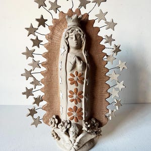 May include: A ceramic statue of the Virgin Mary with a crown, surrounded by stars, and an angel at the base. The statue is painted in shades of brown and white.