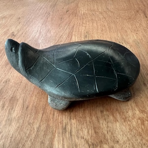 May include: A black carved turtle sculpture with a detailed shell pattern. The turtle is lying on its belly with its head raised.
