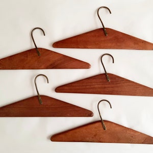 May include: Five wooden hangers with brass hooks. The hangers are all the same size and shape, and they are arranged in a row.